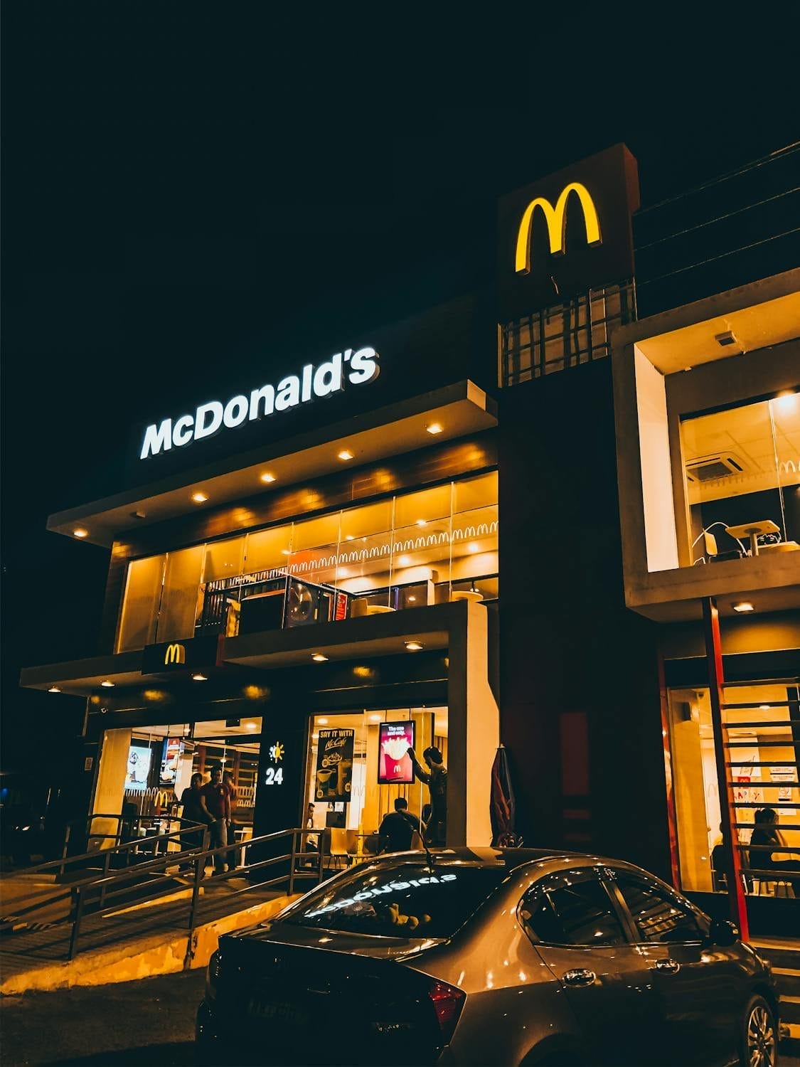 People standing in front of a McDonald’s restaurant at night, illuminated by signage and surrounding lights.
