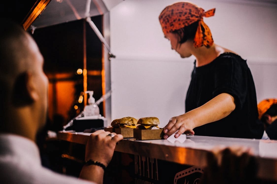 Person serving burgers from a food truck at night, with a customer waiting at the counter.